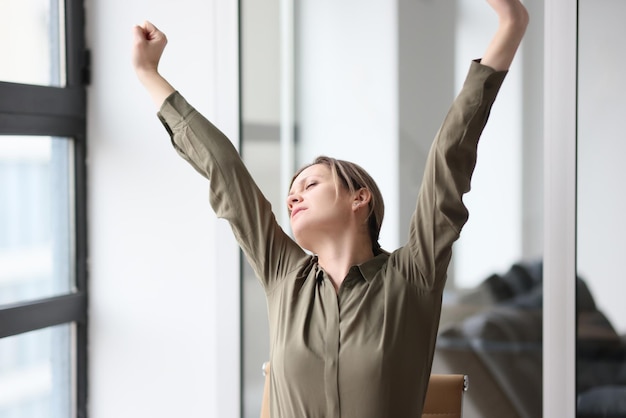 Tired office manager stretches out her hands while sitting at workplace concept of overwork and