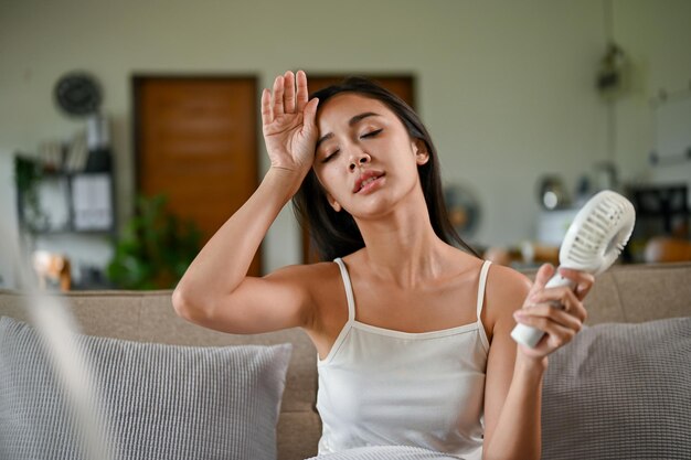 A tired and overheated Asian woman suffering from a heat attack while resting on a couch