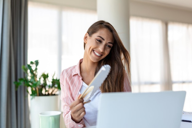 Tired overheated young woman hold wave fan suffer from heat sweating indoor work on laptop at home office annoyed woman feel uncomfortable hot summer weather problem no air conditioner concept