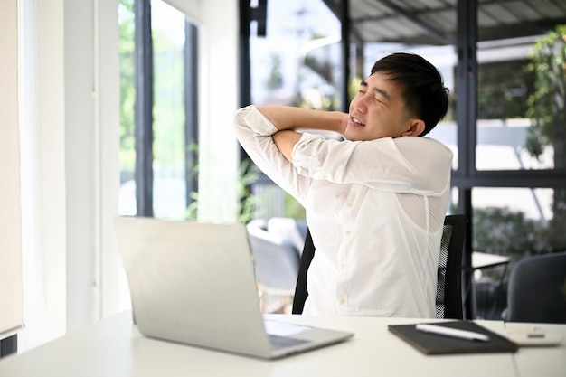 Tired and overworked Asian businessman stretching his arms and rubbing his shoulder