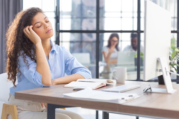 Tired overworked woman resting while she was working on computer Collegues are on the background