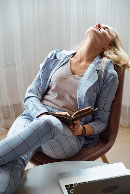 Tired overworked young woman in a suit sitting on a chair in the office