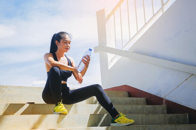 Tired runner woman with a bottle of electrolyte drink freshness after training outdoor workout