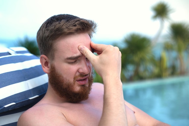 Tired sick exhausted man handsome guy in swimming pool is suffering from hot summer heat stroke