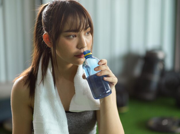 Tired sporty girl taking a rest and drinking a water to hydrated after had a extremely hard workout.