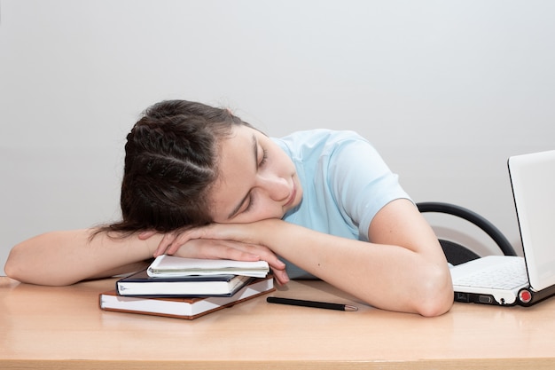 Tired student girl with books and laptop sleeps on the table.