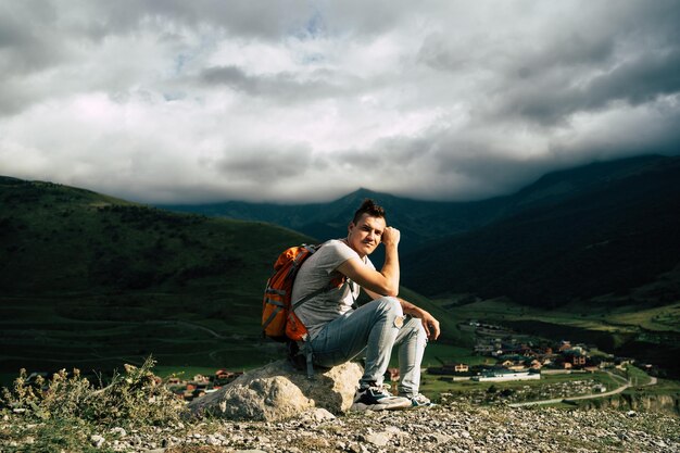 Photo tired traveling man resting on hill exhausted male tourist sitting on stone after active trekking in mountains