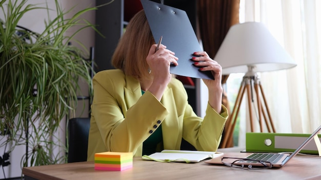 Tired woman covers face with folder of documents bad working mood mood and fatigue concept