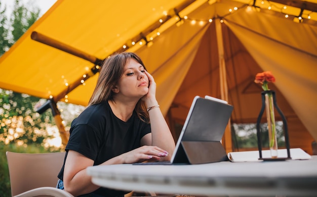 Tired Woman freelancer using a laptop on a cozy glamping tent in a sunny day Luxury camping tent for outdoor summer holiday and vacation Lifestyle concept