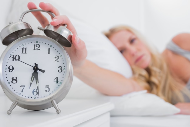 Tired woman turning off the alarm clock 