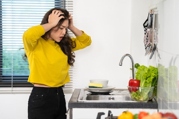 Tired woman washing dishes in the sink in kitchen at home