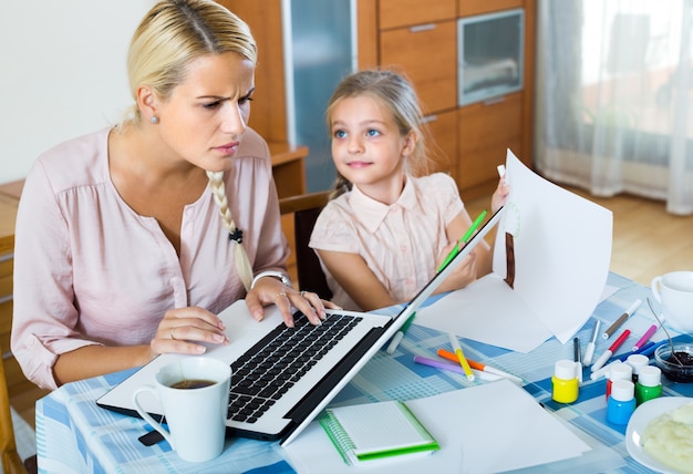 Tired woman with daughter working online&#xA;