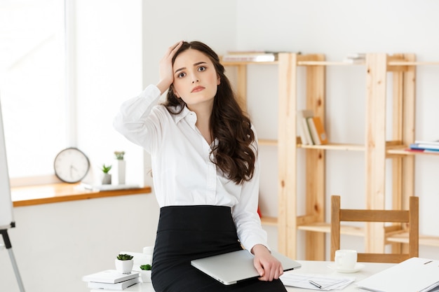 Tired young businesswoman suffering from long time sitting at computer desk in office