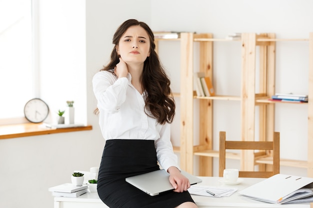 Tired young businesswoman suffering from long time sitting at computer desk in office.