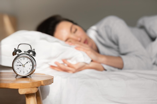 Tired young european lady lies and sleeps on white comfortable bed selective focus on alarm clock on table