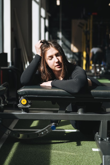 Tired Young fitness brunette woman training on muscles equipment at gym