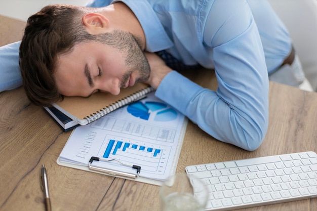 Photo tired young male sleeping sitting with computer behind desk at office