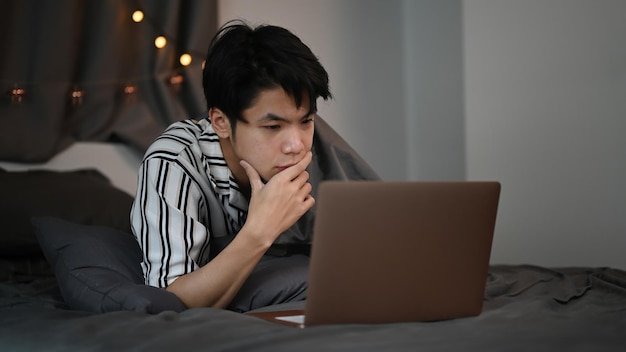 Tired young man under blanket working with laptop computer at late night