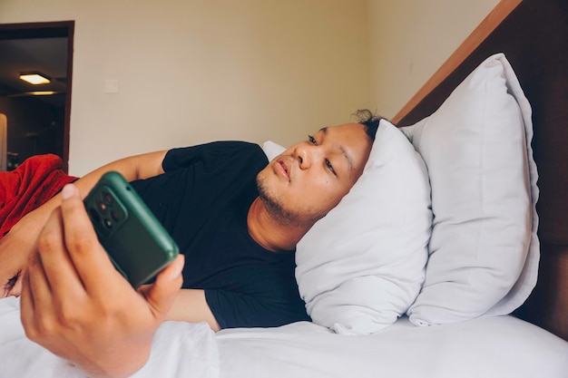 Tired young man checking on his phone while lying in bed