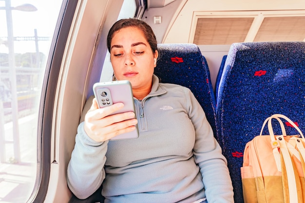 Tired young woman in train watching video in mobile phone