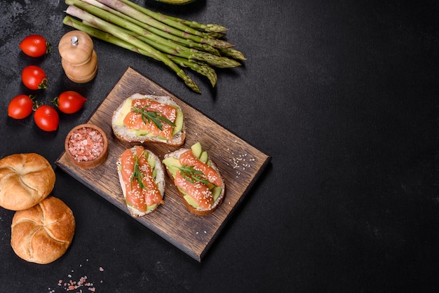 Toast sandwich with butter avocado and salmon decorated with arugula and sesame seeds on a black stone background