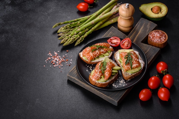 Toast sandwich with butter avocado and salmon decorated with arugula and sesame seeds on a black stone background