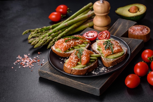 Toast sandwich with butter avocado and salmon decorated with arugula and sesame seeds on a black stone background