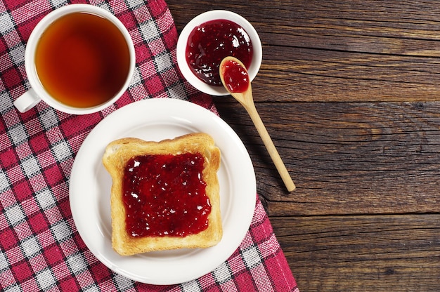 Toast with jam and cup of tea on wooden table covert tablecloth. Top view