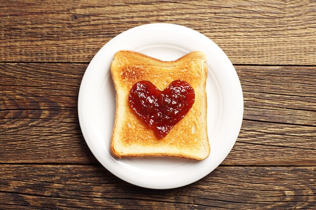 Toast with jam in shape of hearts on wooden background. Top view