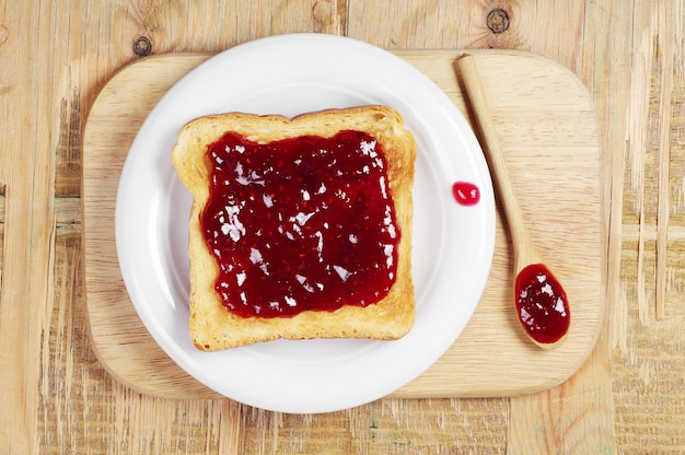 Toast with jam and wooden spoon on cutting board. Top view