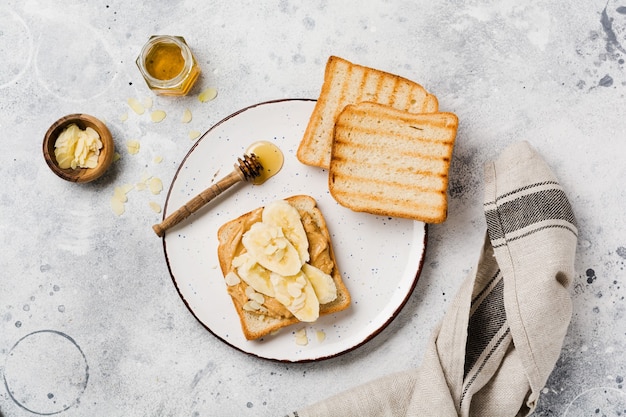 Toast with peanut butter, banana slices, honey and almond flakes on an old gray concrete