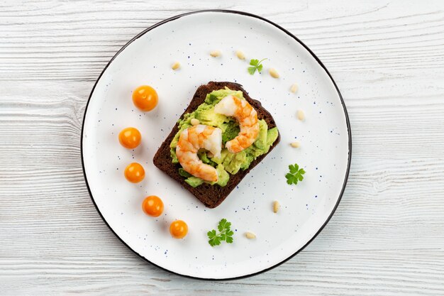 Toast with shrimp, avocado, nuts, physalis, parsley on plate