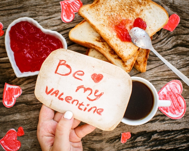 Toast with strawberry jam Be My Valentine white message card with coffee in hands Valentine's Day