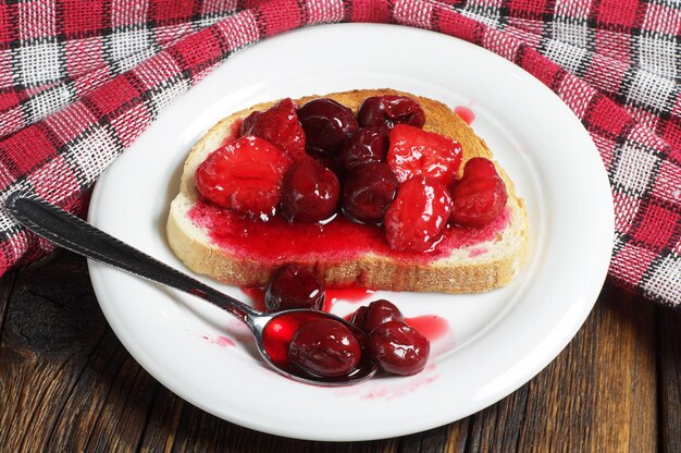 Toasted bread with canned cherries and strawberries on rustic wooden table