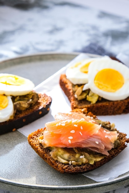 Toasted breads with boiled eggs, avocado and salmon. Guacamole sandwiches. Healthy breakfast. Sesame seeds. Vegetarian healthy eating.