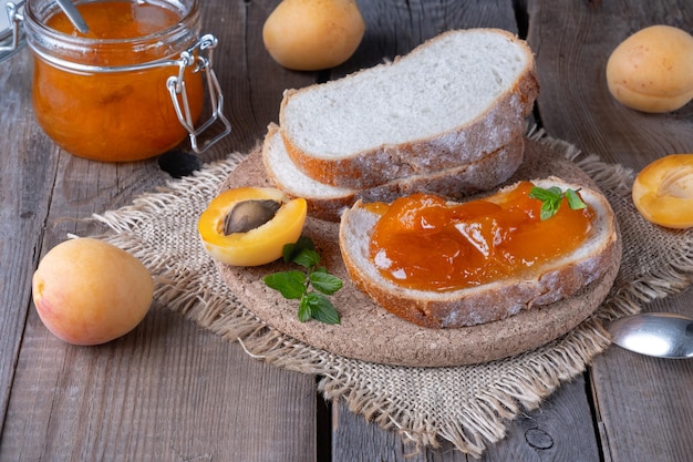 Toasts of bread with apricot jam and fresh fruits with mint on an old wooden table Tasty breakfast