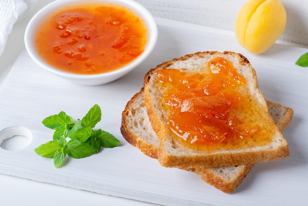 Toasts of bread with apricot jam and fresh fruits with mint on white wooden table Tasty breakfast