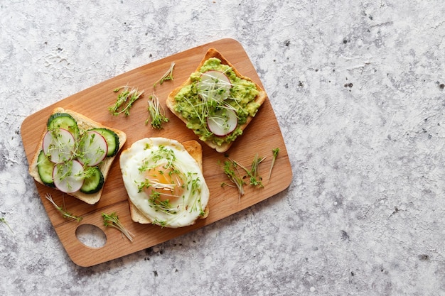 Toasts or bruschetta with egg cucumber radish avocado and microgreens on the table Tasty breakfast