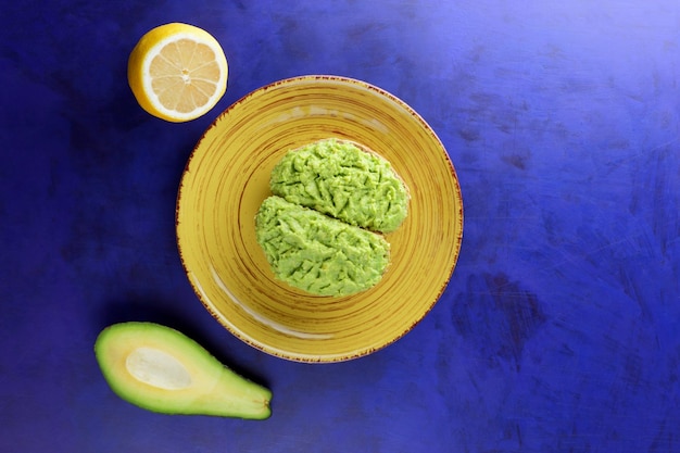 Toasts and green avocado and yellow lemon on a blue background Healthy breakfast toasts with avocado smash on a yellow plate Vegetarian food concept Closeup