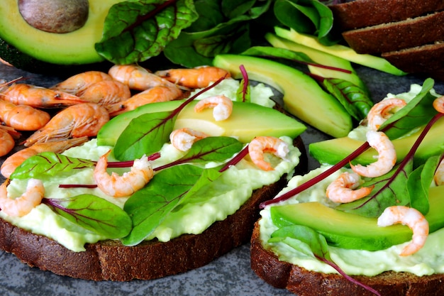 Toasts with avocado paste, prawns and chard. Healthy eating. Useful vegetarian open sandwiches with avocado and shrimp. Salad chard. Vegetarian foods. Superfoods.