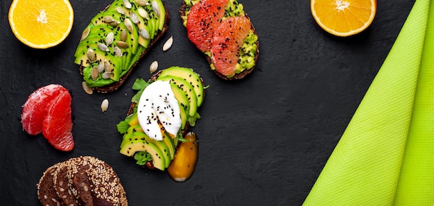 toasts with avocado, sesame seeds, grapefruit, orange, egg and coffee on a concrete black background. delicious breakfast with coffee and toasts