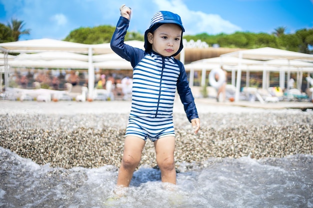 Toddler boy in a swimming suit plays with pebbles on the seashore in a hotel