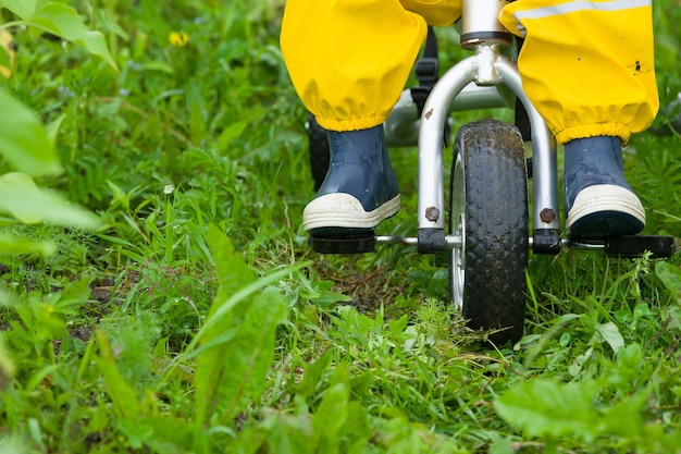 Toddler child feet in rubber boots and pants riding a bicycle on green grass Boy walking outdoors