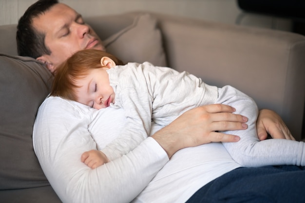 Toddler and dad sleeping on the couch during the day concept childrens day and parental care focus on the hands