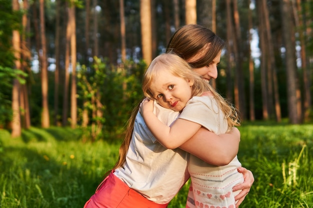 Toddler daughter hugs her mother tightly while walking in nature