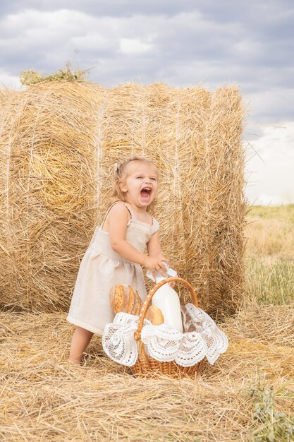 toddler girl blond in linen dress takes bottle of milk from the bread basket