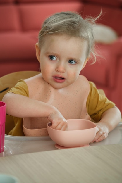 Toddler girl eating happily in high chair food at home