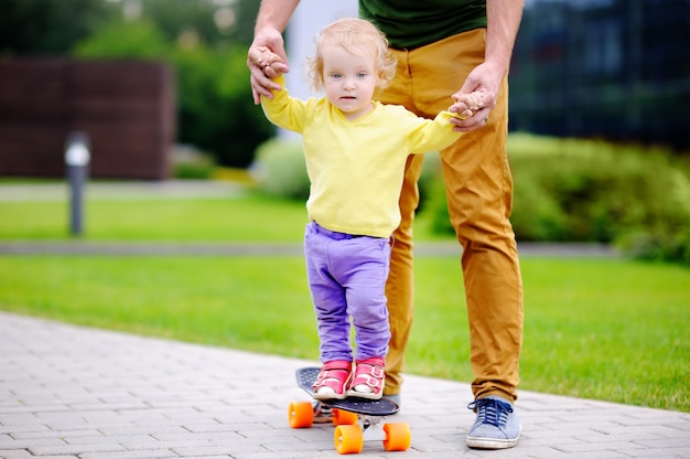 Toddler girl learning to skateboard with her father