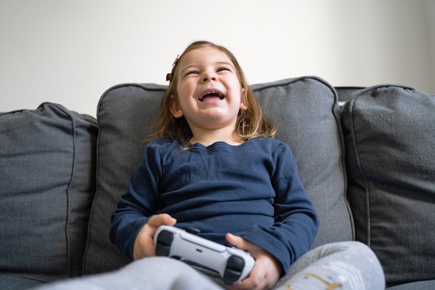 Toddler girl playing video game console at home in living room on the sofa