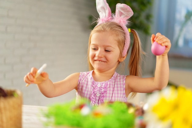 Toddler girl with bunny ears coloring eggs for Easter